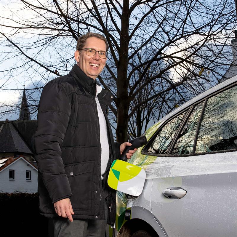 Wethouder Mark Gerritsen staat naast een elektrische auto met de laadkabel in zijn handen. 